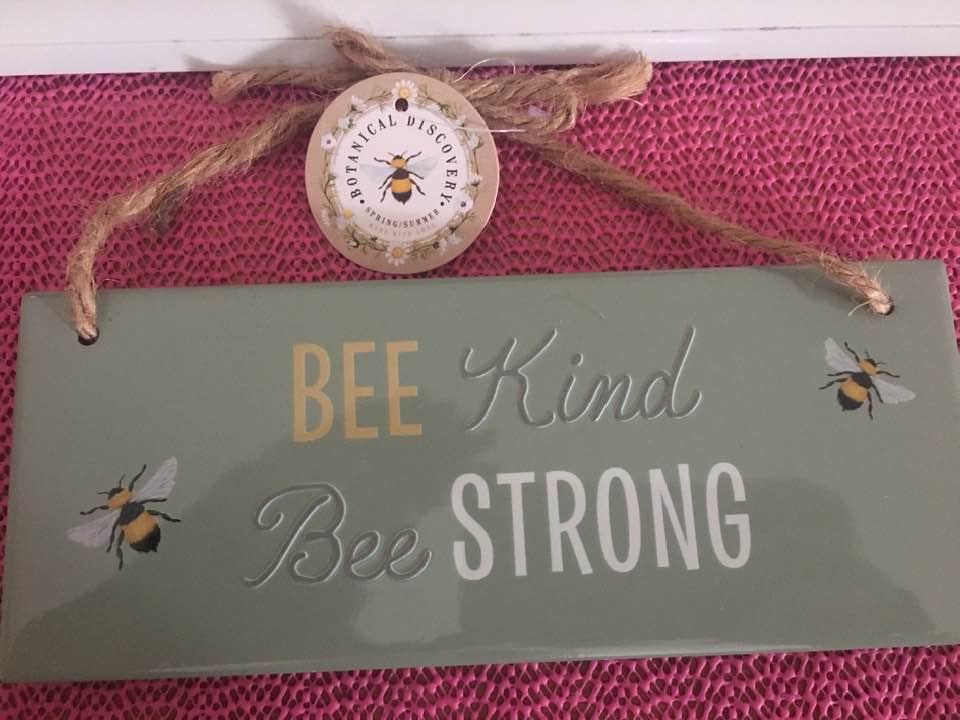 ceramic hanging sign with bee kind and bee strong message displayed on a wooden surface